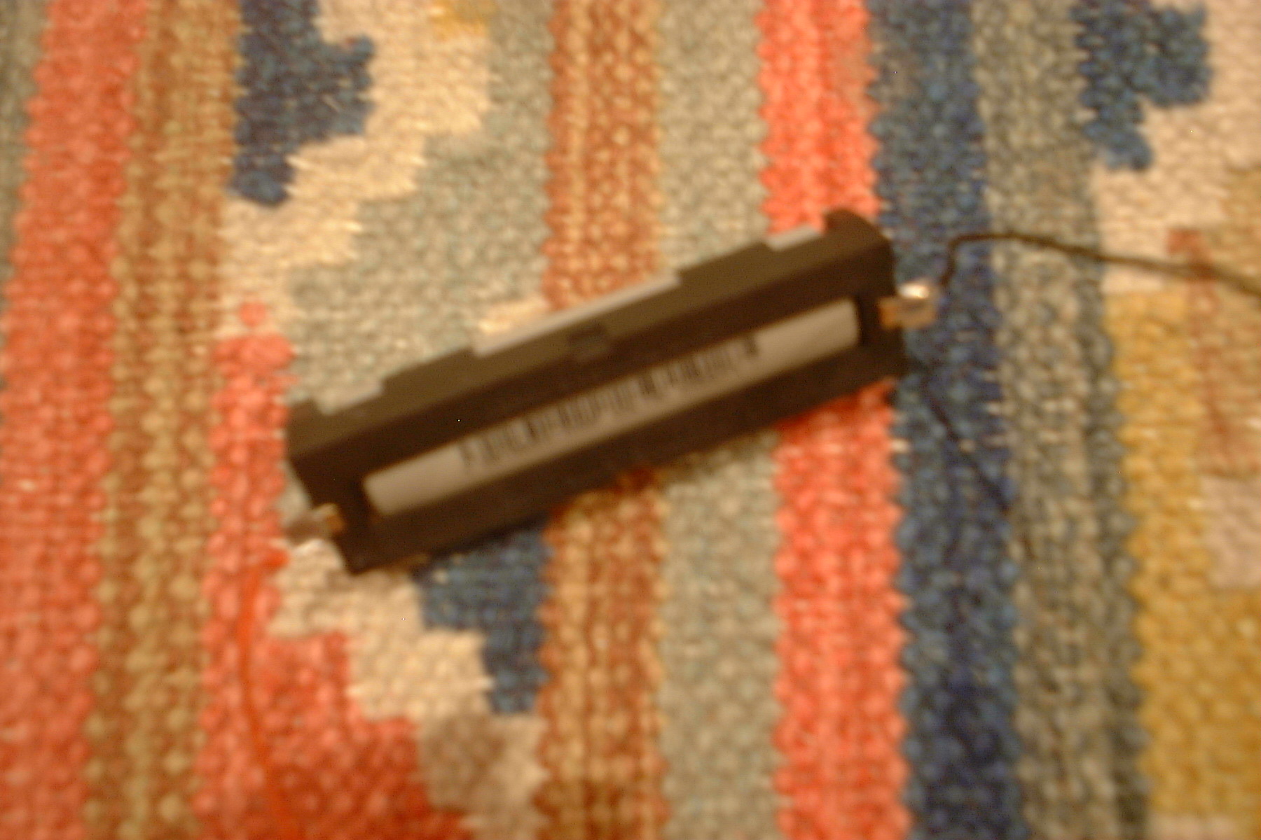 a photo of a 18650 battery cell, it sits in a small battery seat with a wire coming off either end. Its backed by a colorful carpet