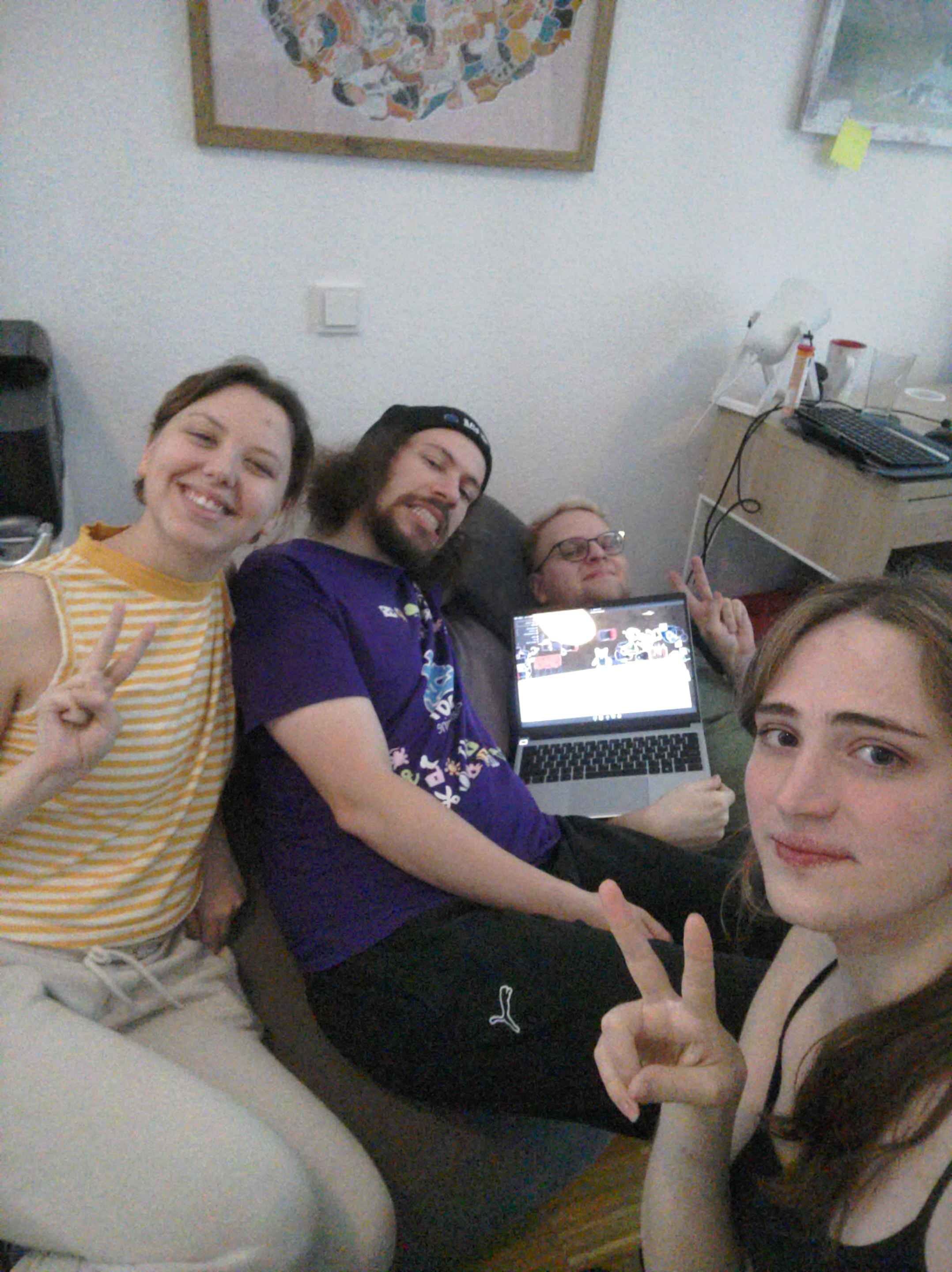 A photo of 4 people, one holding a laptop showing a video game, they are posing and smiling