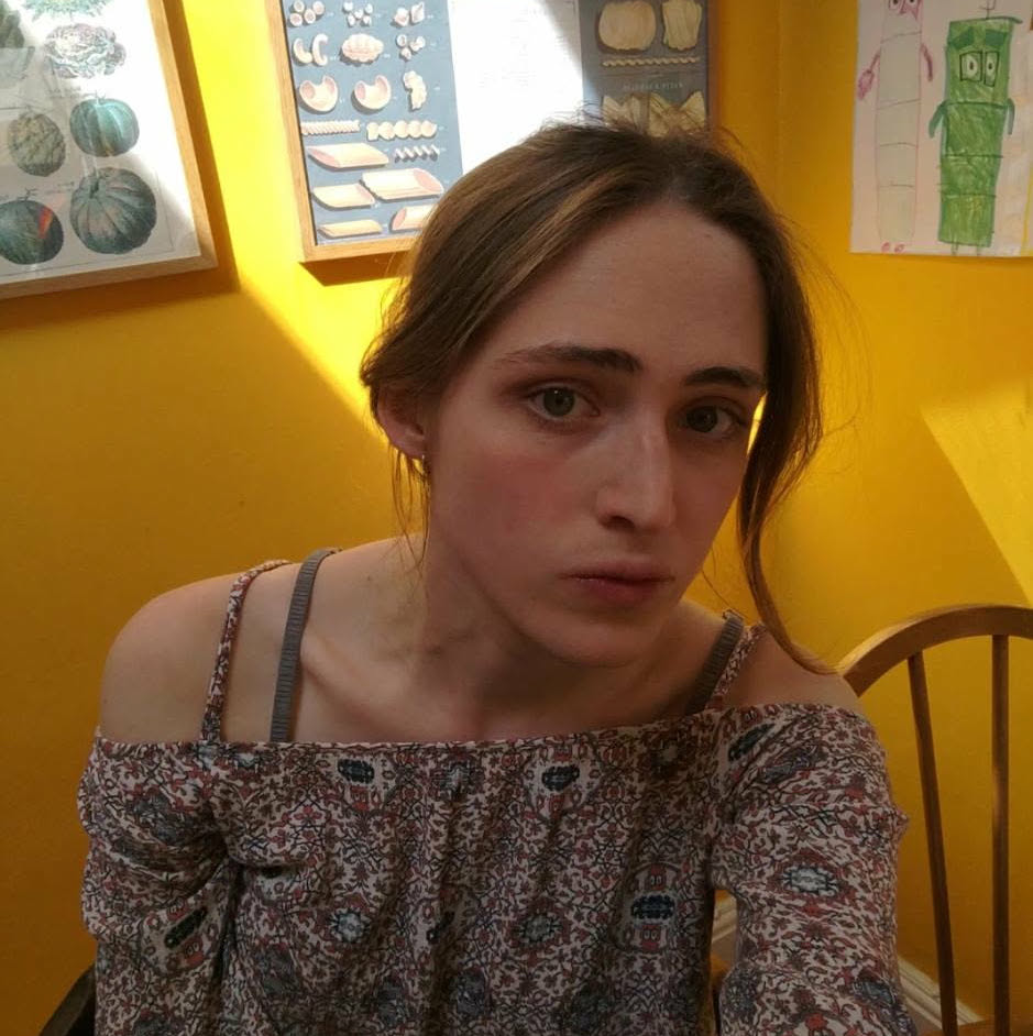 A photo of me, I am wearing a summer outfit in a room with yellow walls and lots of sunlight. My hair is long and tied back.